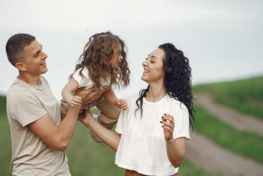 A joyful family moment outdoors with parents playing with their daughter.